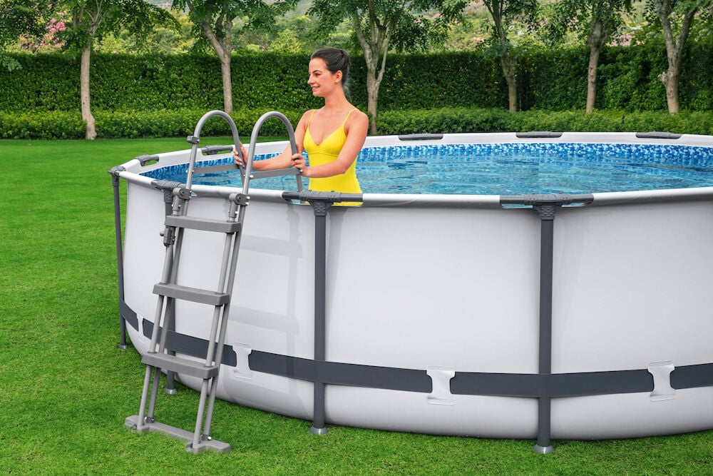 Frame-Pool, Komplettset 13030 Liter GS, mit Frau in gelbem Badeanzug an grauer Leiter.