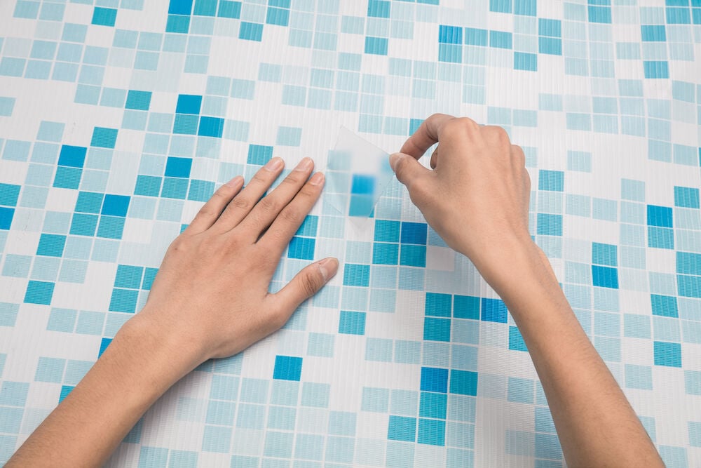 Hånd påfører selvklebende lappelapp på bassengliner.