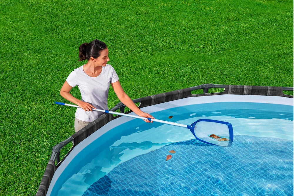 Nainen puhdistaa altaan pintaa pitkällä haavilla.