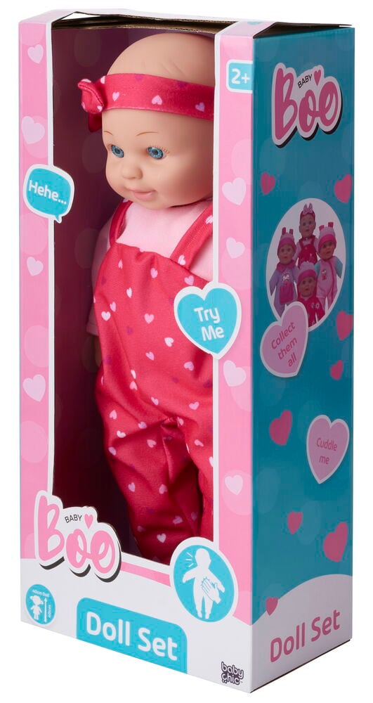 Eine Babypuppe mit blauen Augen, rosa Schleifenstirnband, hellrosa Top und rotem Herz-Overall.
