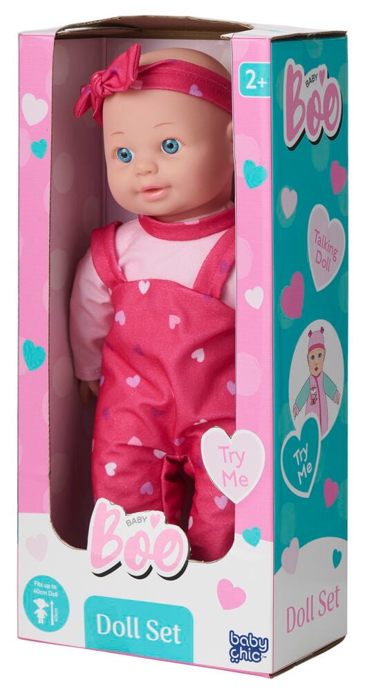 Eine Puppe Baby Boo 40 cm in rosa Hemd, rosa herzgemusterter Latzhose und rosa Haarband, im Karton gezeigt.