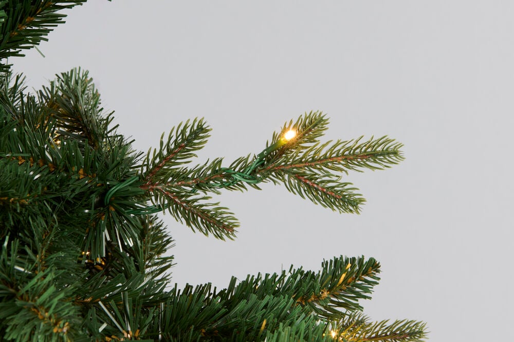 Nærbilde av en grønn kunstig juletregren med integrerte varmhvite LED-lys.