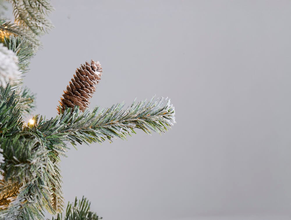 Nærbilde av en frostet juletregren med en brun kongle og varme hvite LED-lys.