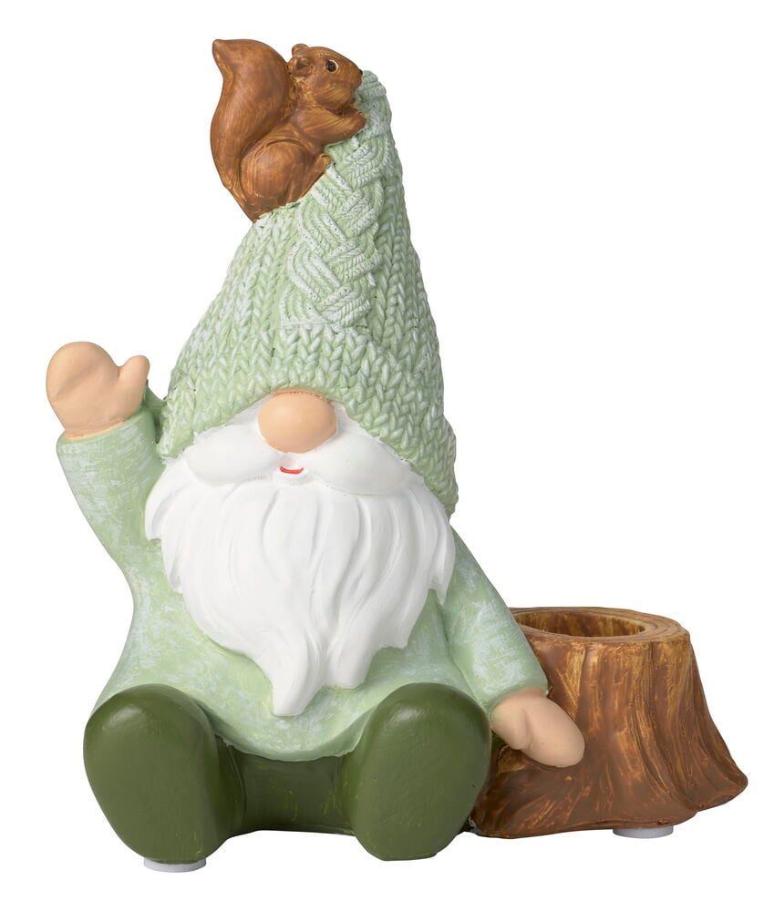 Grön tomtefigur med ekorre på mössan och vitt skägg, bredvid brun trästubbe julljusstake.