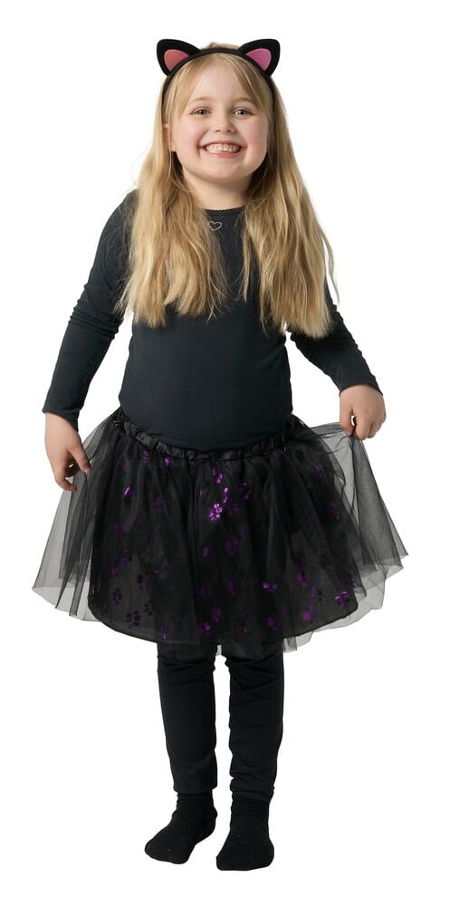 Barn bär svart katthuvudband, svart tyllkjol med lila mönster, svart topp, leggings och strumpor.