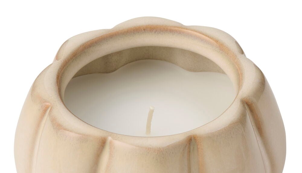 Närbild av ett ljusbeige pumpaformat doftljus i keramik med vitt vax och en veke.