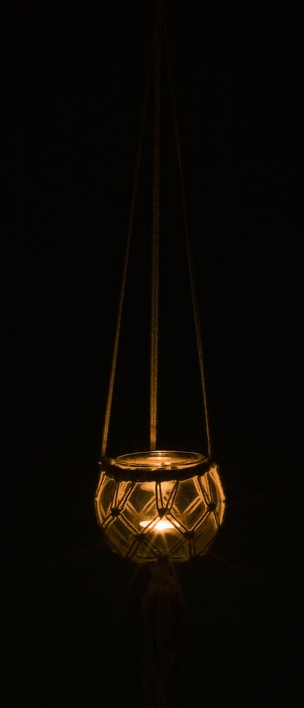 Riippuva lasilyhty käsin solmitulla makrameella ja elävällä kynttilällä.