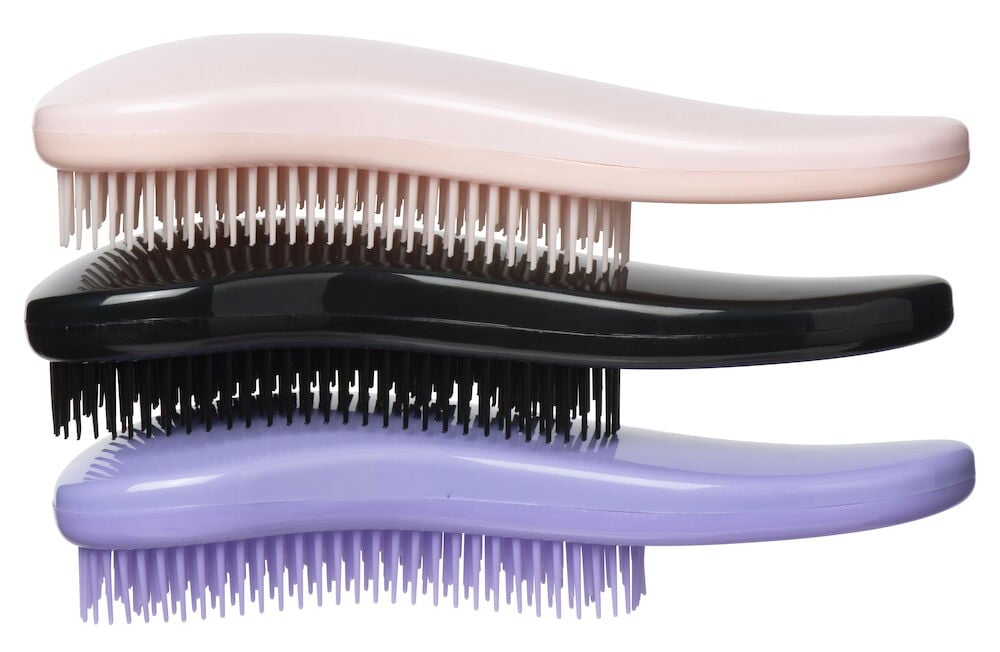 Kolme ergonomista hiusharjaa, väriltään vaaleanpunainen, musta ja violetti.