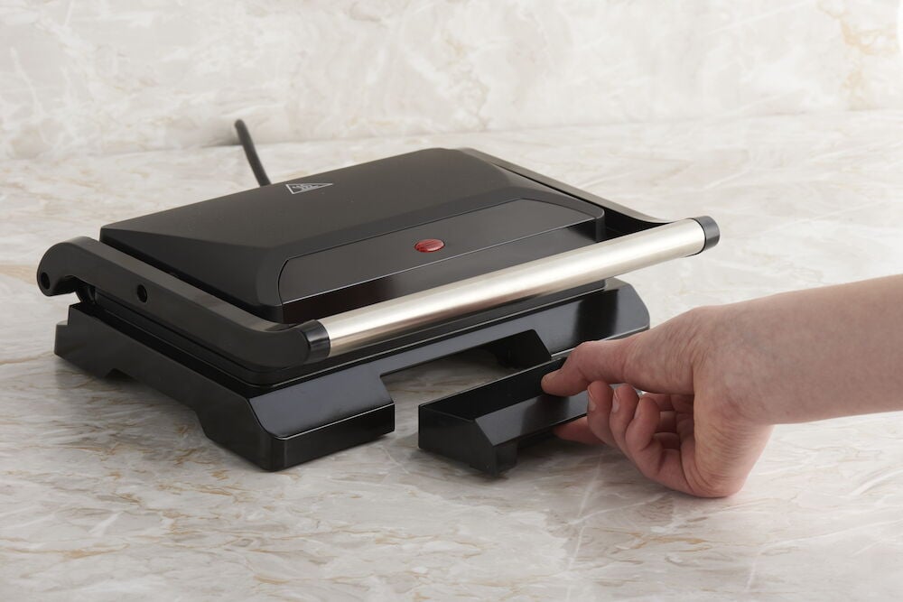 Musta monitoimigrilli, jossa tippalautanen ja hopeanvärinen kahva.