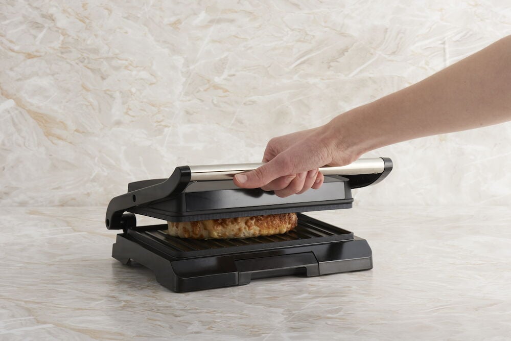 Musta multigrilli, jossa on voileipä ja käsi kannessa.