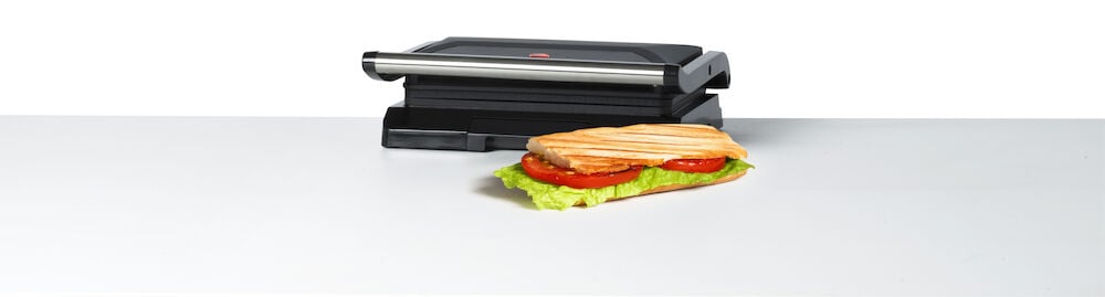 Musta monigrilli voileivällä valkoisella pinnalla.