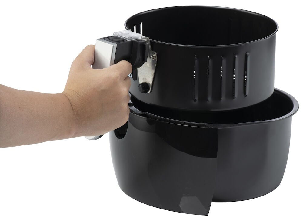 Hand håller svart airfryer-korg med handtag.
