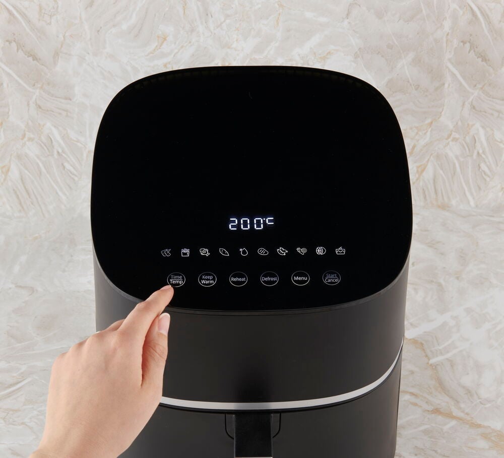 Hand trycker på digital skärm på svart airfryer.