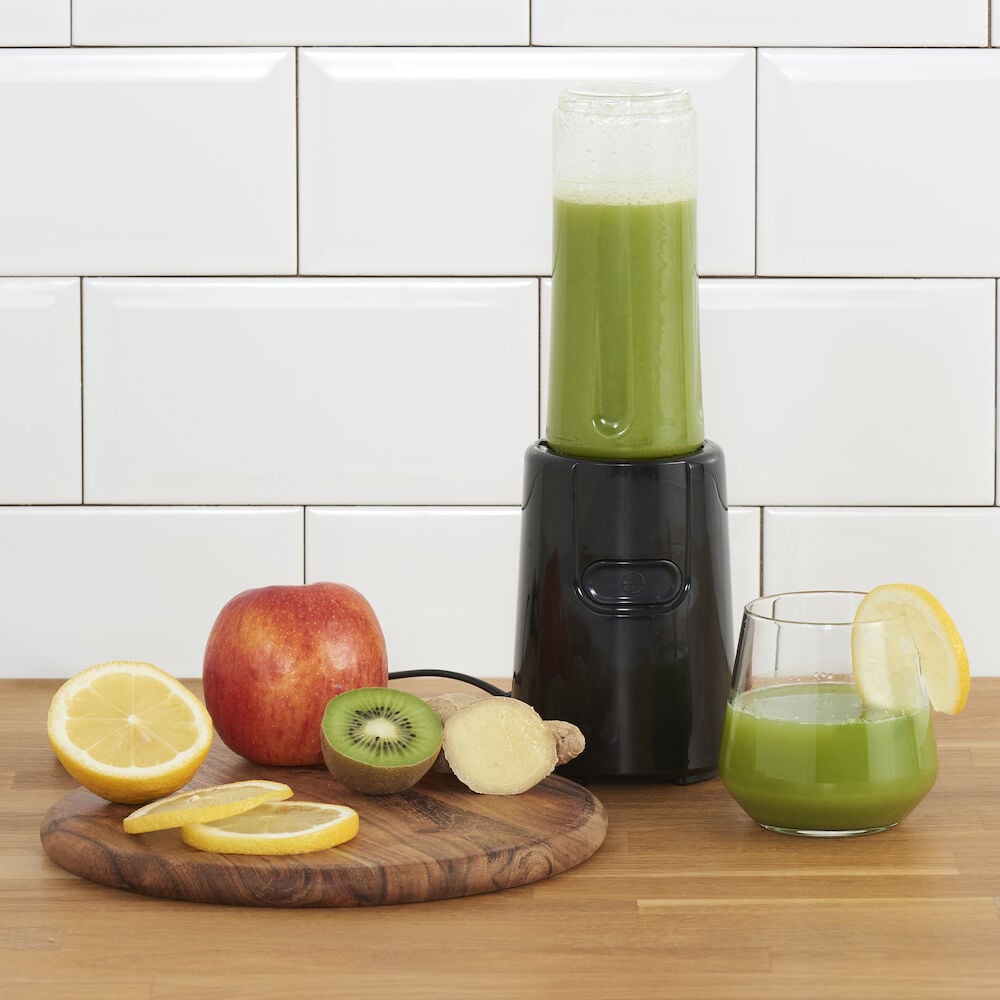 Svart blender med grön smoothie och färska frukter.