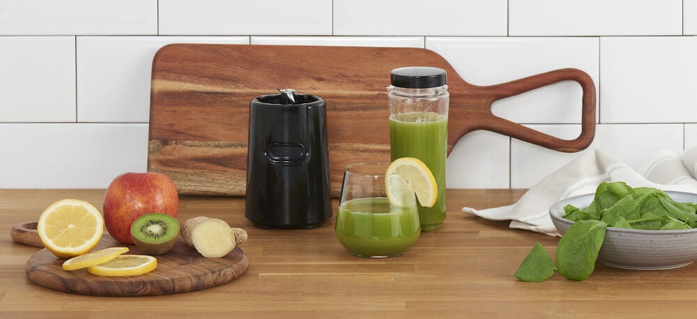 Svart kompakt blender med grön smoothie och frukt.