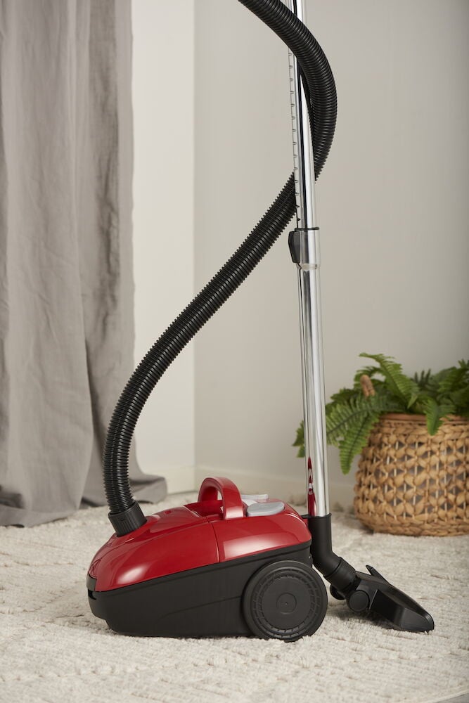 Röd dammsugare med slang på ljus matta.