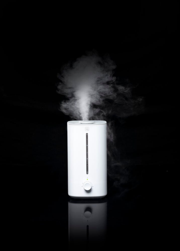 Vit luftfuktare med ånga mot svart bakgrund.