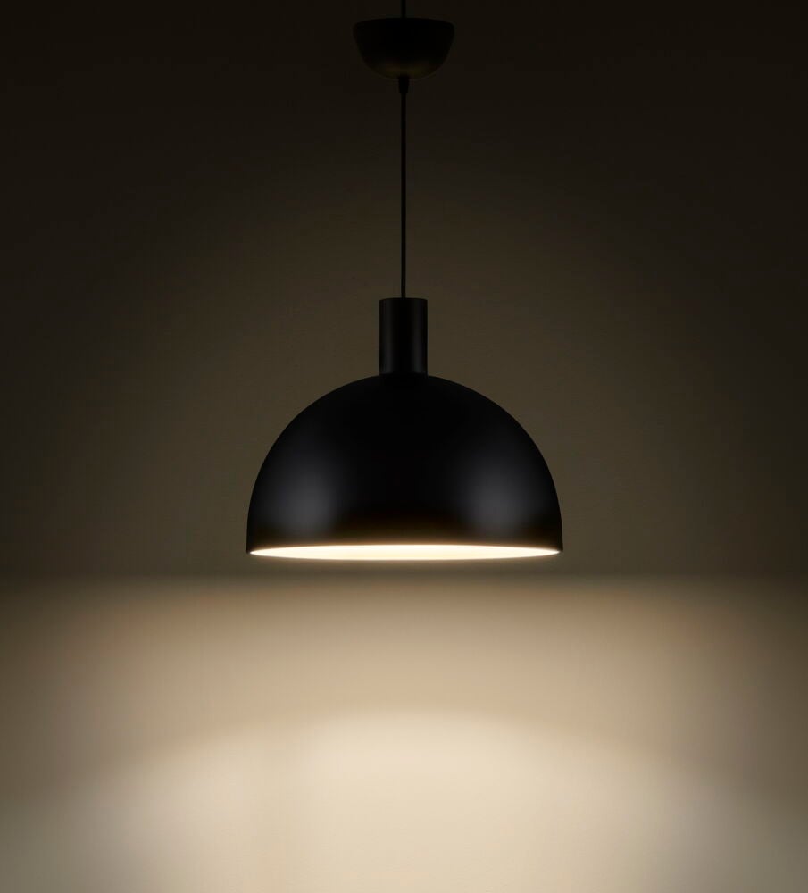 Svart taklampa i metall lyser nedåt mot bord.