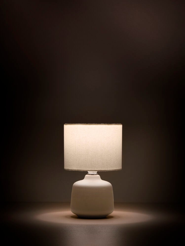 Beige bordslampa med cylindrisk vit linneskärm.