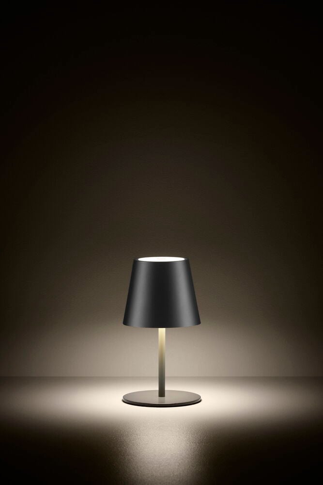 Svart uppladdningsbar bordslampa lyser på mörkt underlag.