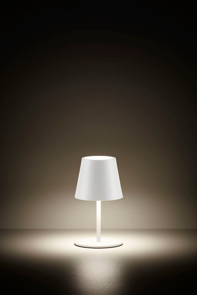 Vit uppladdningsbar bordslampa lyser i mörkt rum.