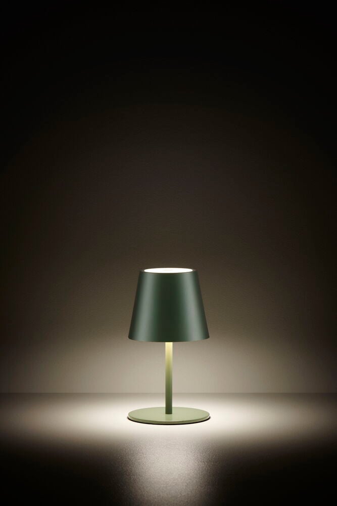 Grön uppladdningsbar bordslampa lyser på mörkt bord.