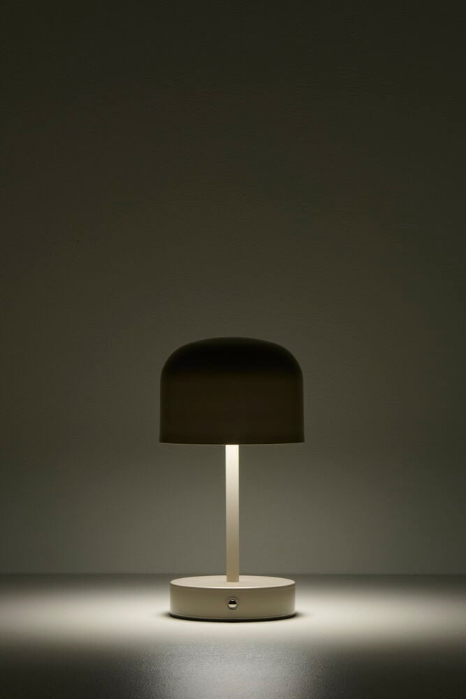 Beige uppladdningsbar bordslampa lyser på mörkt bord.