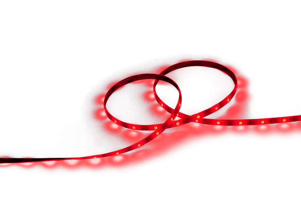 LED-list Ambiance 5 m Flerfärgad ligger slingrad och lyser rött på en vit yta.