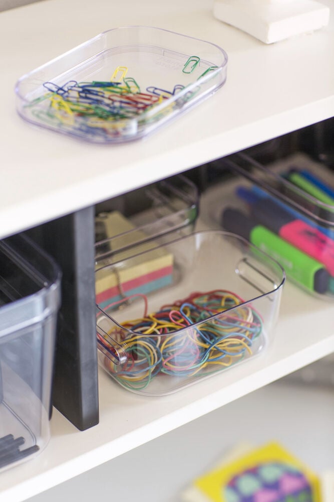 Läpinäkyvä säilytyslaatikko, jossa klemmareita ja kuminauhoja.