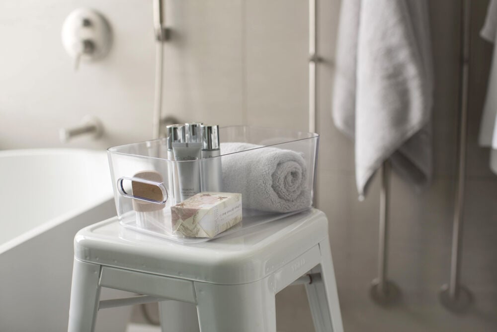 Transparent förvaringslåda med handtag och badrumsartiklar.