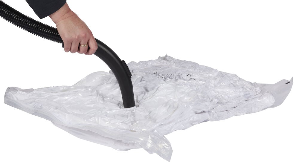 Hand trycker dammsugare mot genomskinlig vakuumpåse.