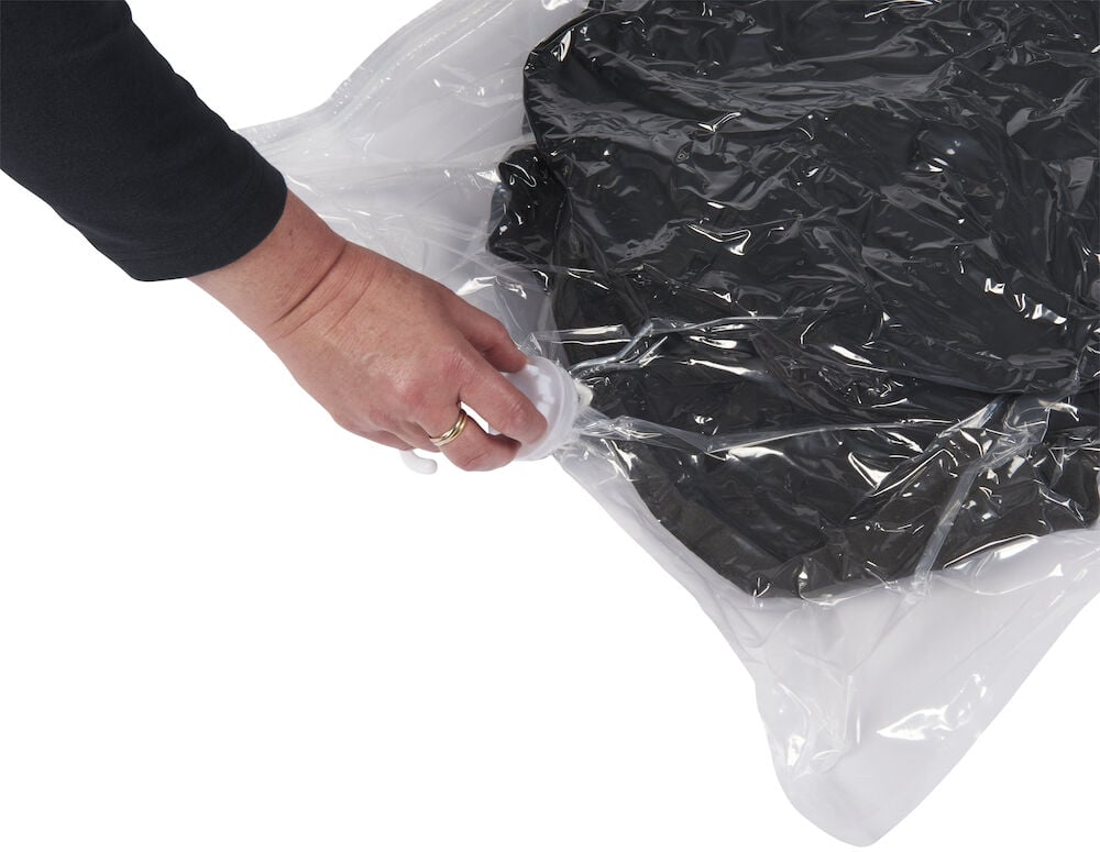 Käsi puristaa ilmaa ulos läpinäkyvästä tyhjiöpussista.