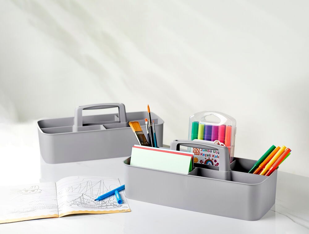 Harmaa säilytyslaatikko, jossa on kahvat ja erilaisia toimistotarvikkeita.
