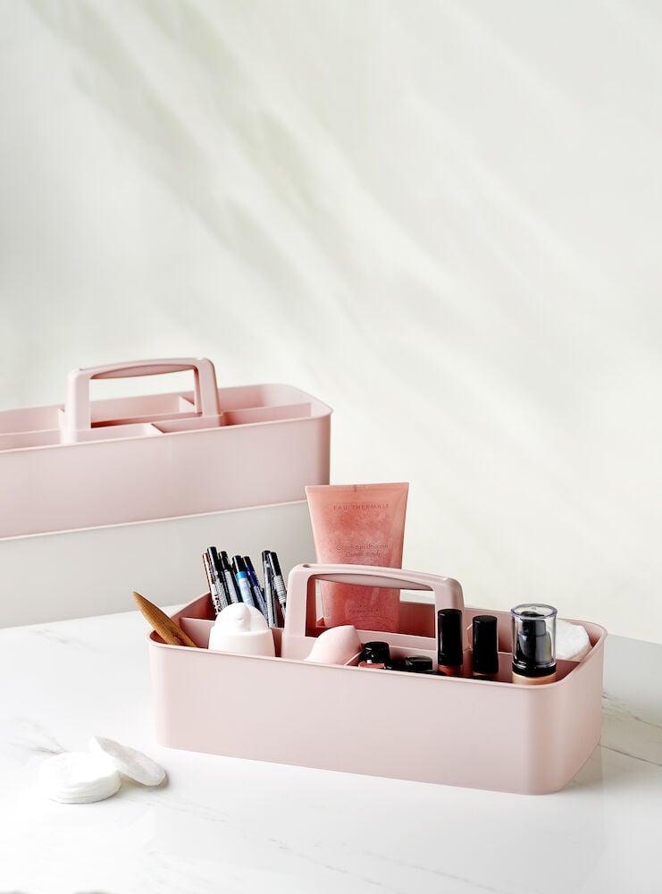 Vaaleanpunainen säilytyslaatikko, jossa on kahvat ja meikin lisätarvikkeet.