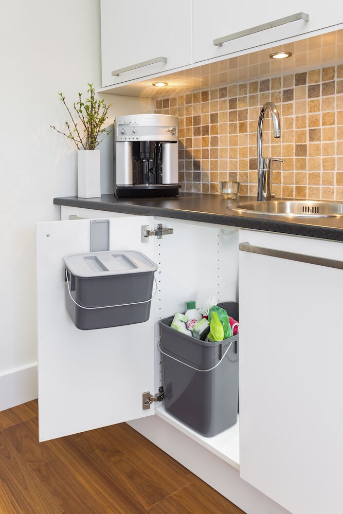 Tre grå återvinningskärl med lock i köksskåp.