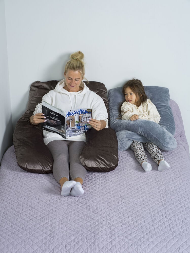 Kaksi henkilöä istuu vartalotyynyt sylissään sängyllä.