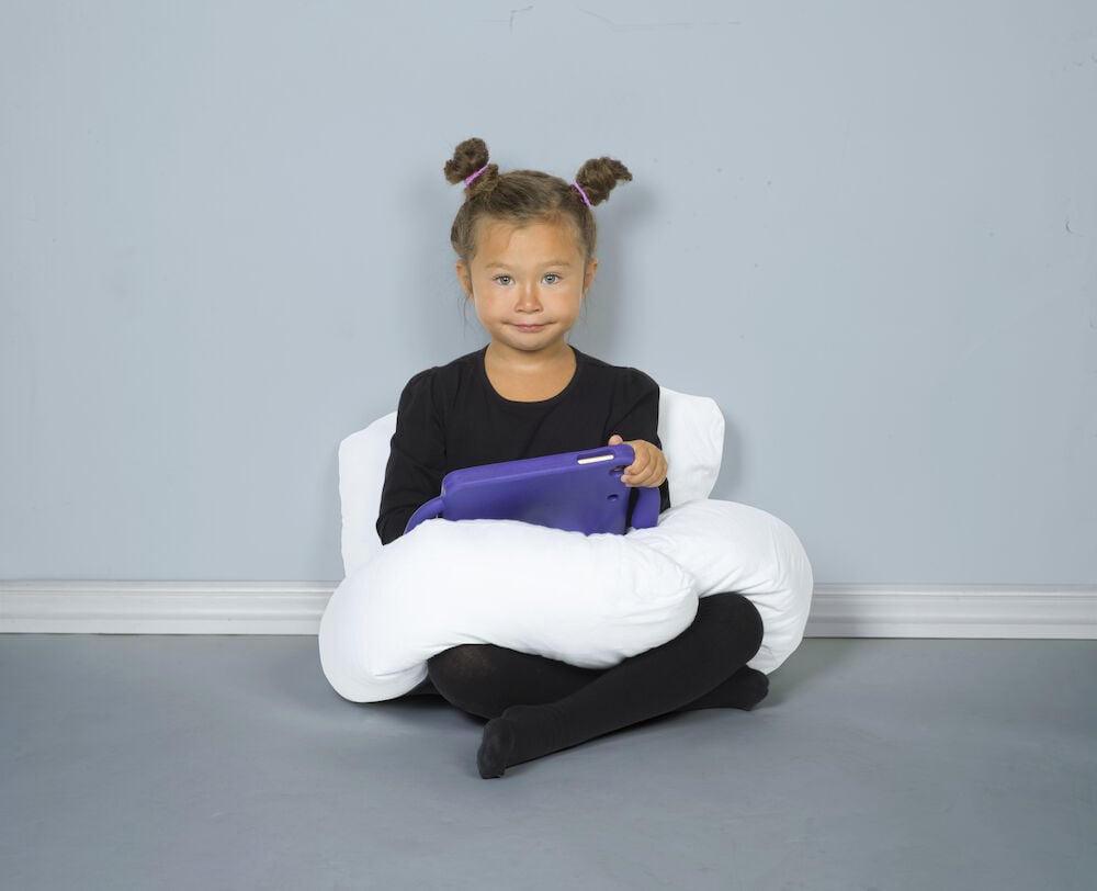 Lapsi istuu valkoisen U-muotoisen vartalotyynyn ja tabletin kanssa.