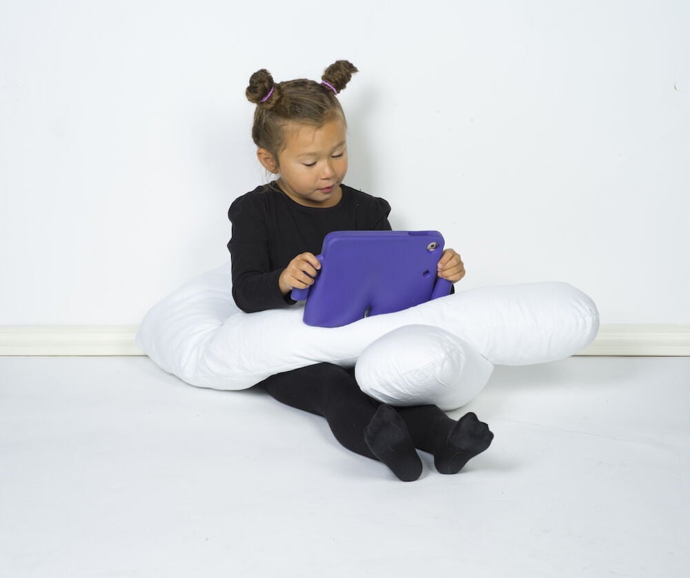 Lapsi istuu U-muotoisen valkoisen vartalotyynyn ja tabletin kanssa.
