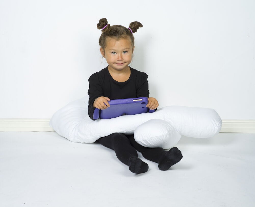 Lapsi, jolla on vartalotyyny ja tabletti sylissään.