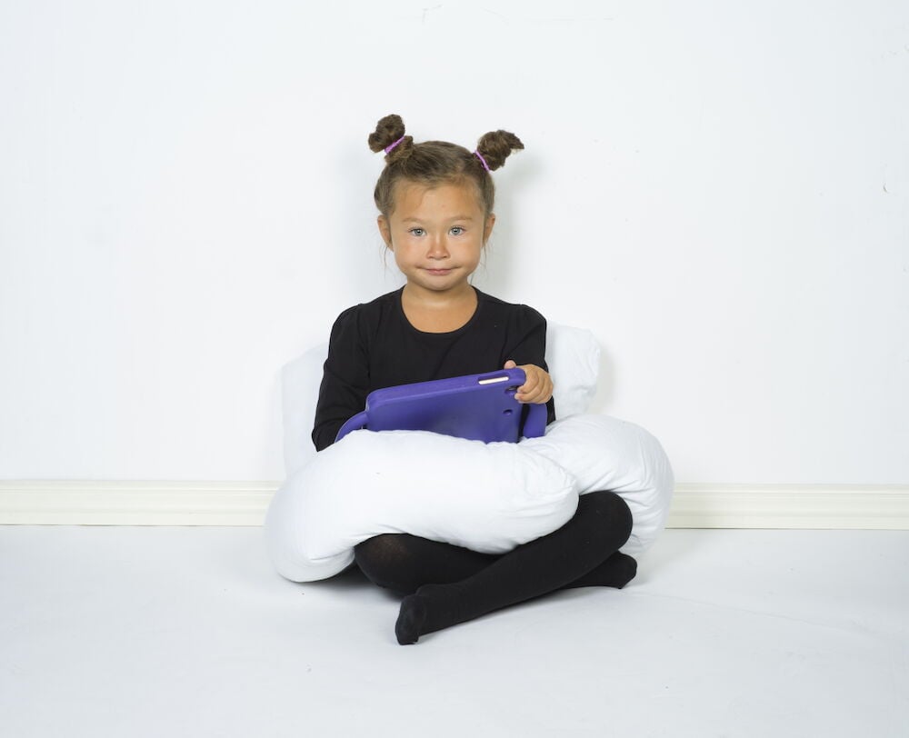 Lapset istuvat lattialla tyynyjen ja tablettien kanssa.