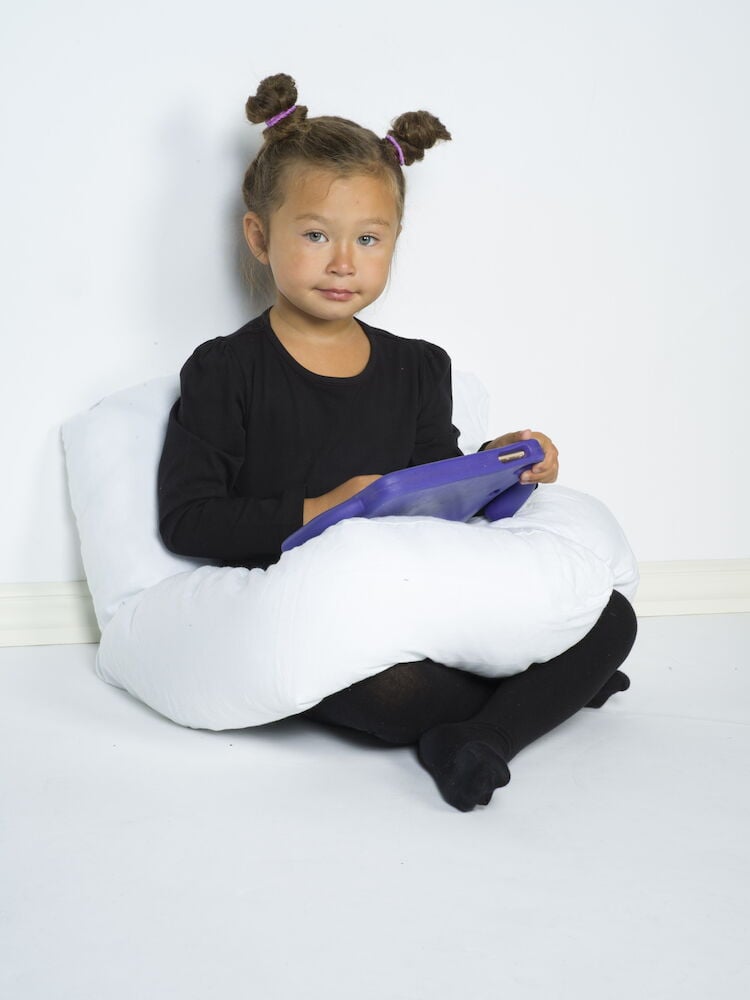 Lapsi istuu valkoisen U-muotoisen vartalotyynyn päällä.