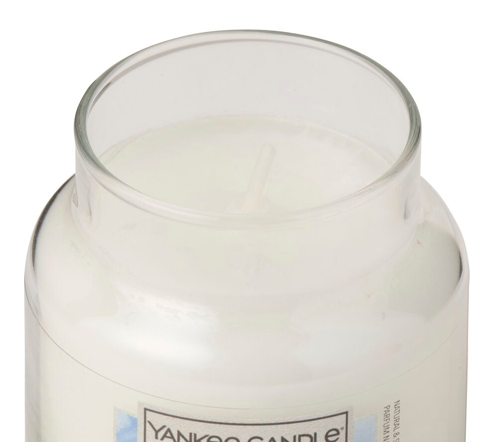 Et hvitt duftlys i et klart glass med en synlig veke, sett ovenfra.