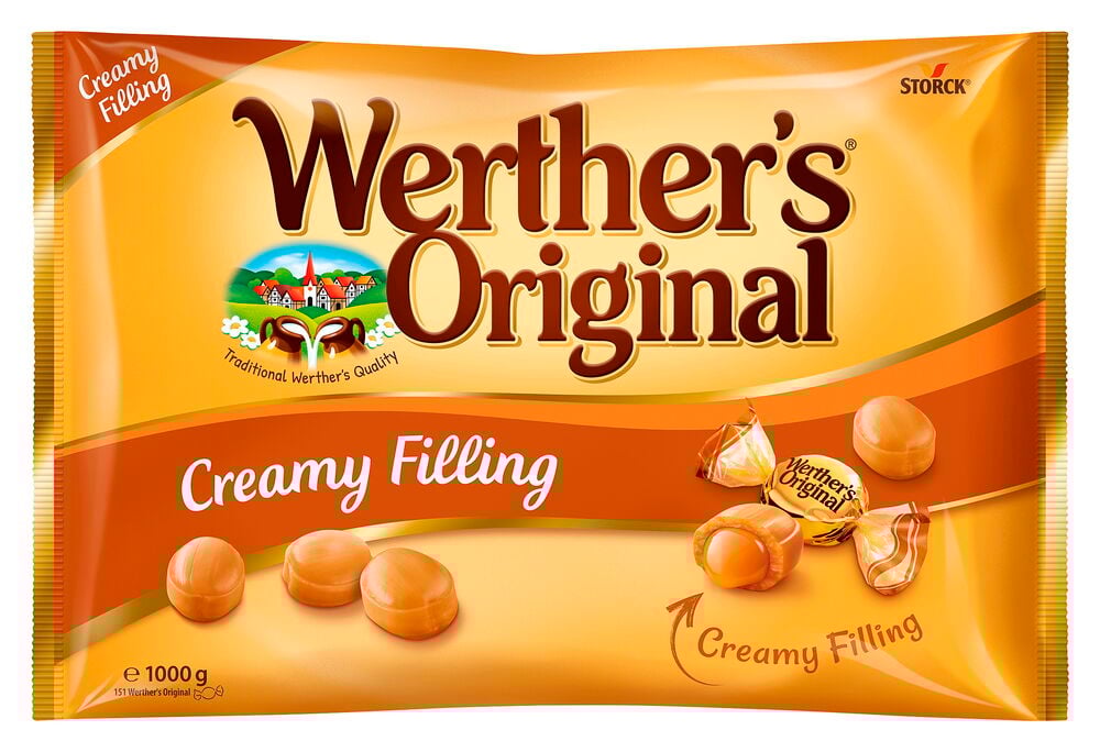 Suuri oranssi pussi 1 kg pehmeätäytteisillä karamelleilla, useita kääreestä otettuja karkkeja esillä.