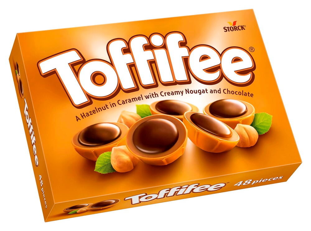 Sjokolade Toffifee 400 g eske med godteri, hasselnøtter og blader på en oransje bakgrunn, sett ovenfra.