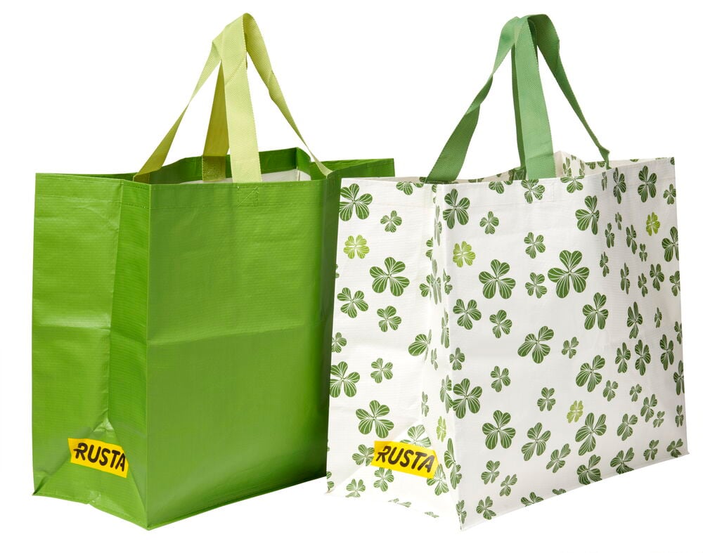 Kaksi uudelleenkäytettävää Ostoskassi Medium Kevät: toinen yksivärinen vihreä, toinen valkoinen vihreillä apilakuvioilla.