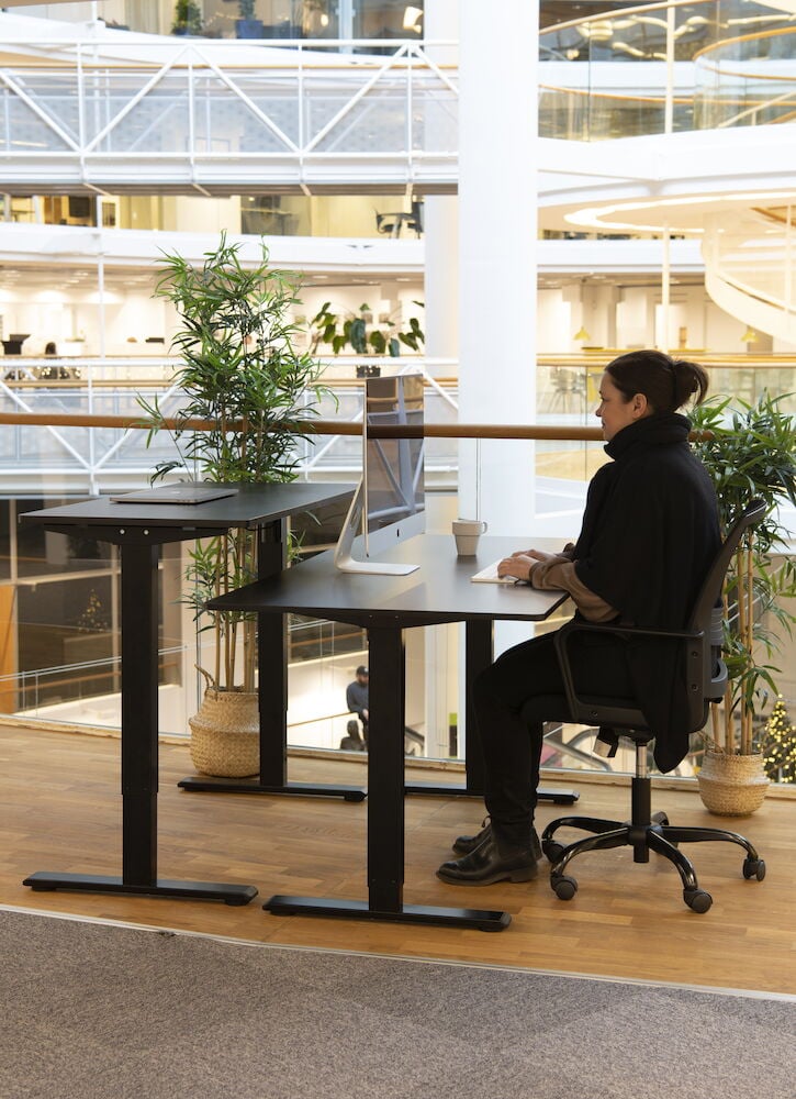 Schwarzer höhenverstellbarer Schreibtisch mit Computer und Stuhl.