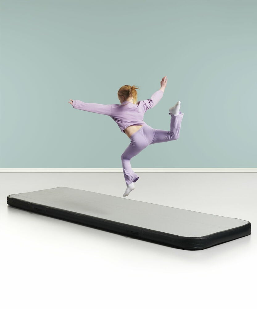 Jente hopper på svartgrå gymnastikkmatte innendørs.