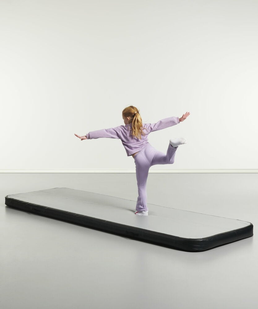 Jente balanserer på grå airtrack gymnastikkmatte.