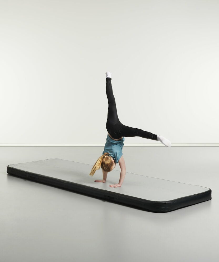 Jente gjør en kollbøtte på blå airtrack-matte.