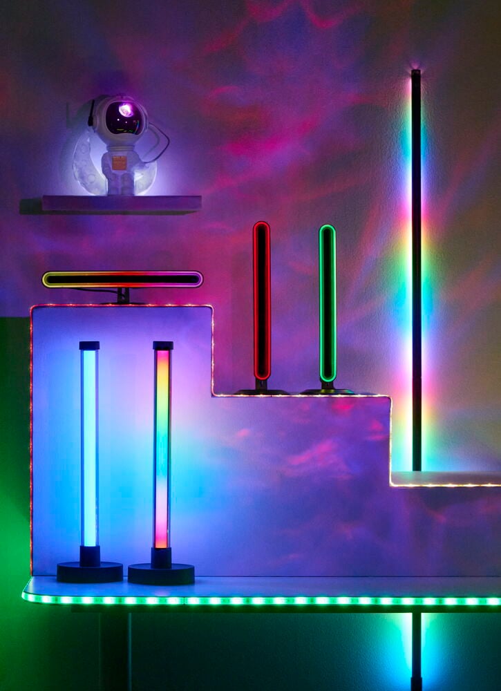 Golvlampa LED Ambiance Flerfärgad, en hög regnbågsfärgad lampa, plus andra LED-lampor och en astronautprojektor.